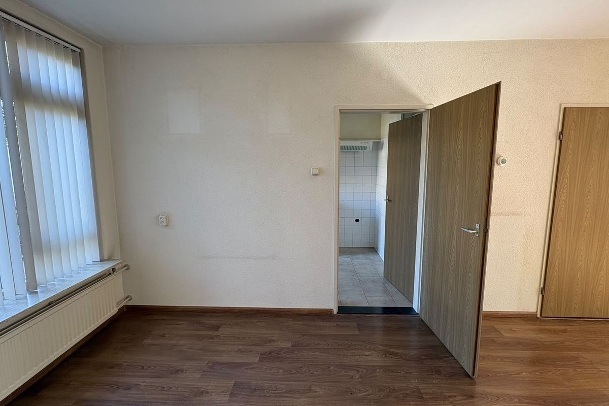 Woonkamer met de dragende binnenwand nog dicht, met een deur naar de keuken