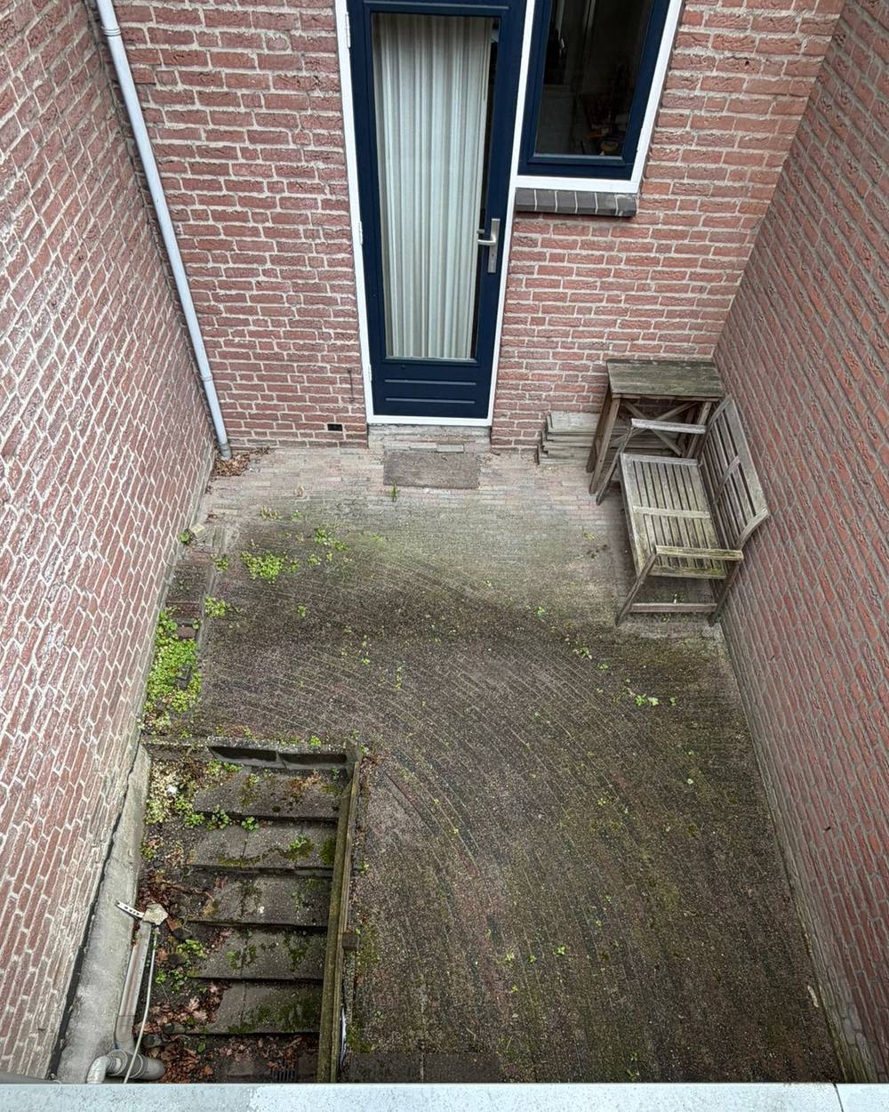 De ingesloten patio zoals hij was, een bemoste vloer tussen twee bakstenen muren