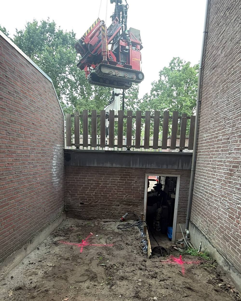 Een kraan tilt een compacte heistelling over de schutting een ingesloten patio in