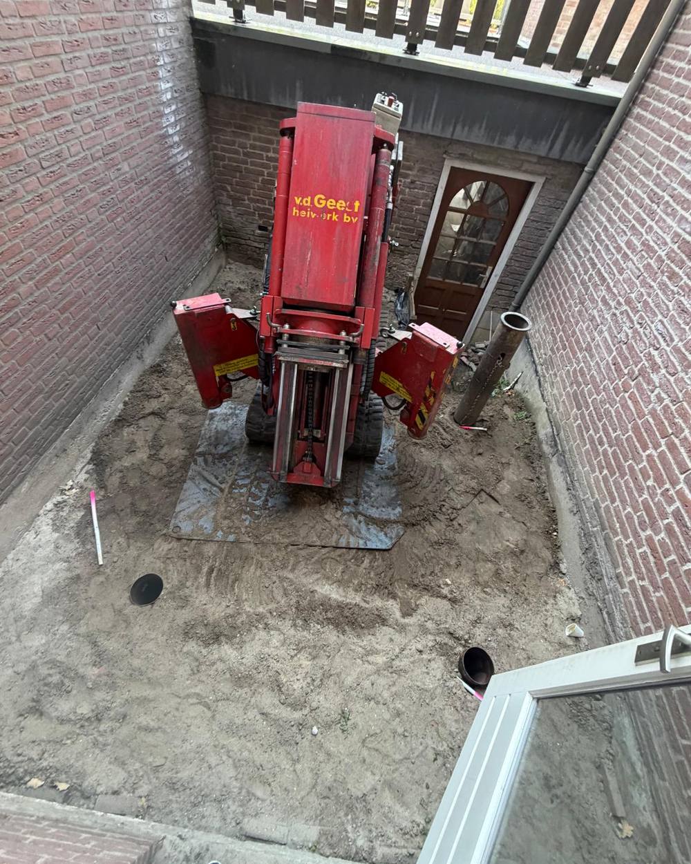 De heistelling opgesteld in de smalle patio, met de stalen buispalen ernaast klaar om geheid te worden